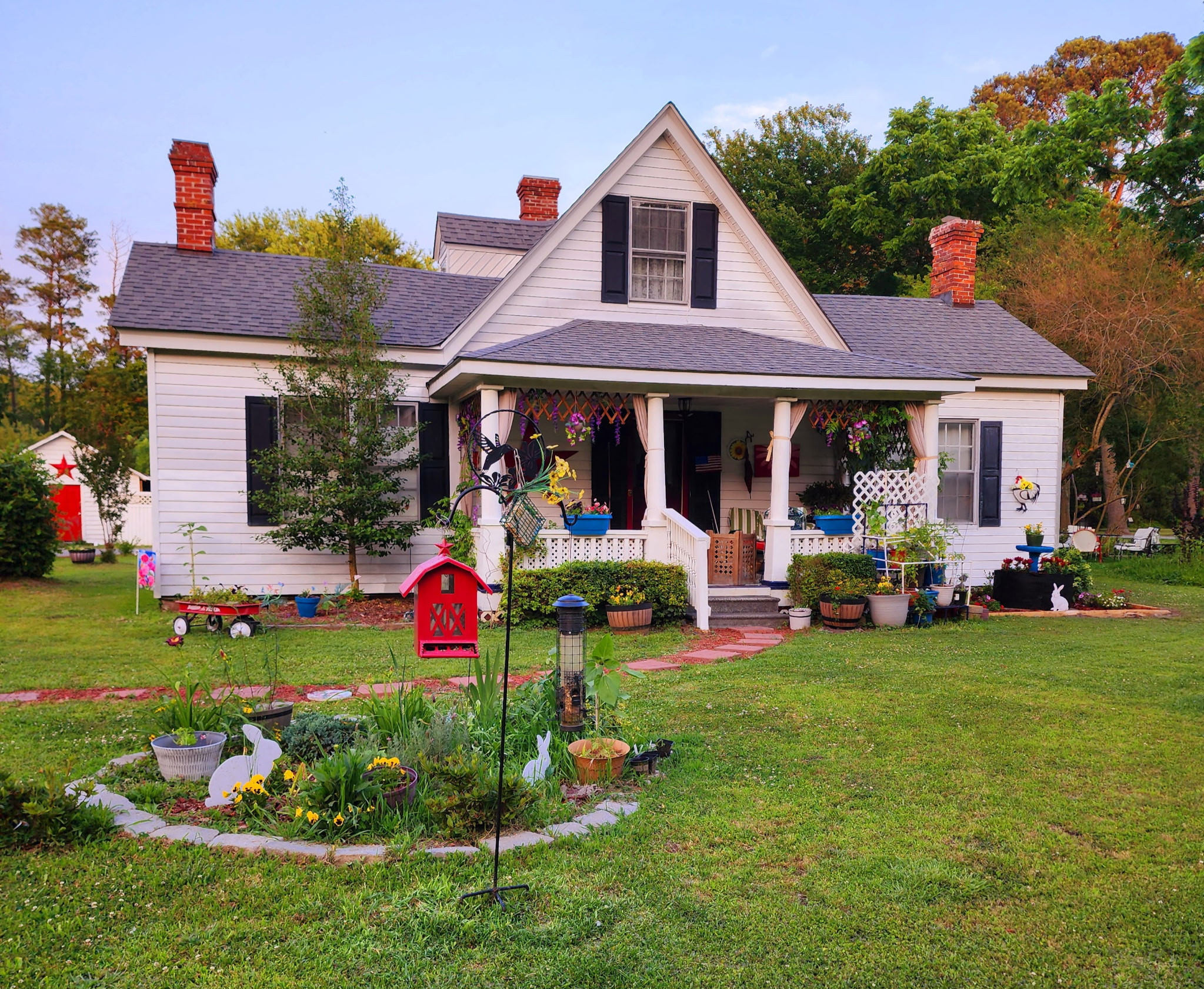 White farmhouse-style home with a front porch, dark shutters, and a large red star on the siding, set on a grassy lawn with trees framing the view belonging to Sponsored Residential Provider Angela Justice in Mathews, Virginia.