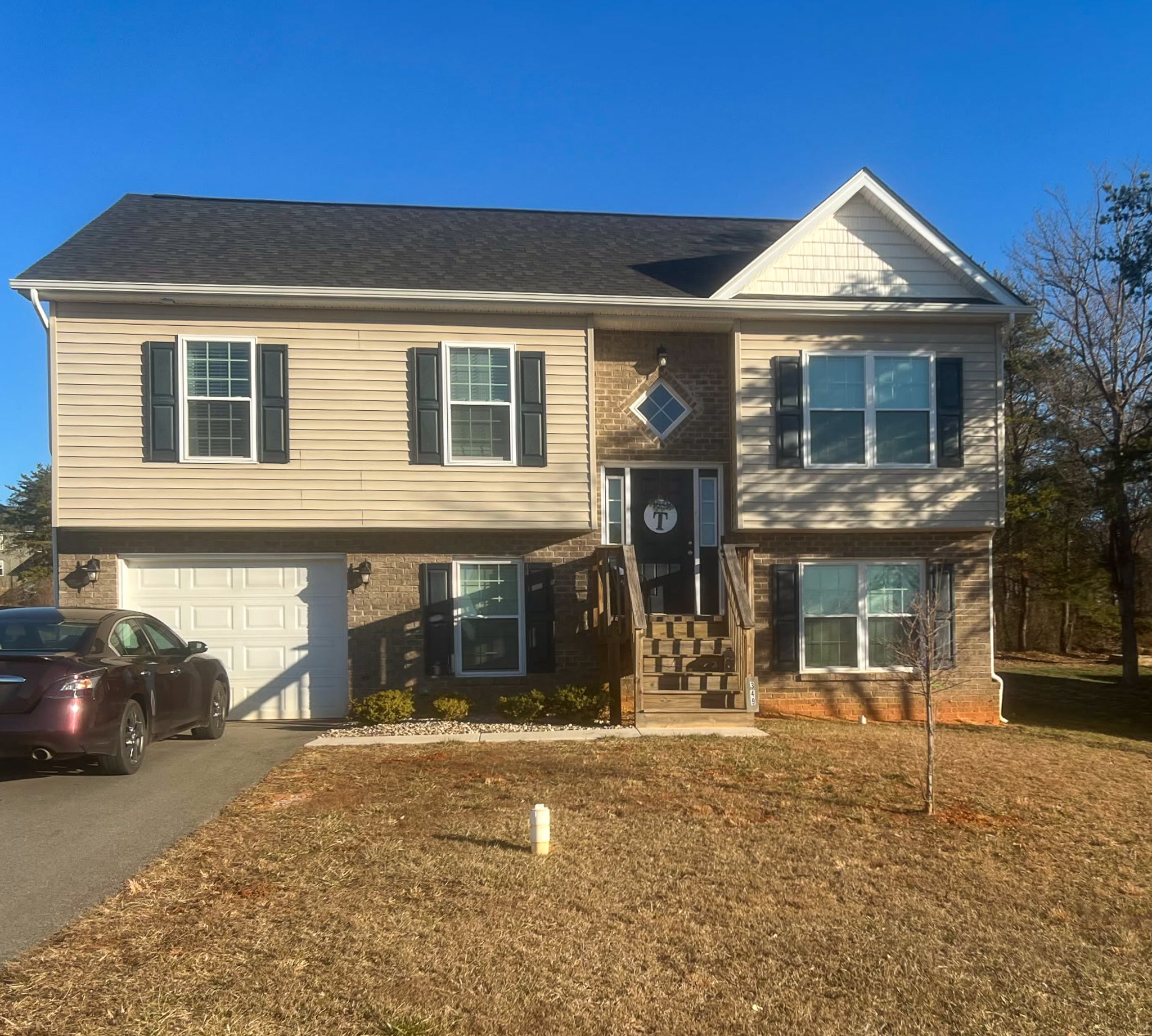 Two‑story beige house with black shutters, a front porch, and an attached garage, photographed on a sunny day belonging to Sponsored Residential Provider Tinika Denson.