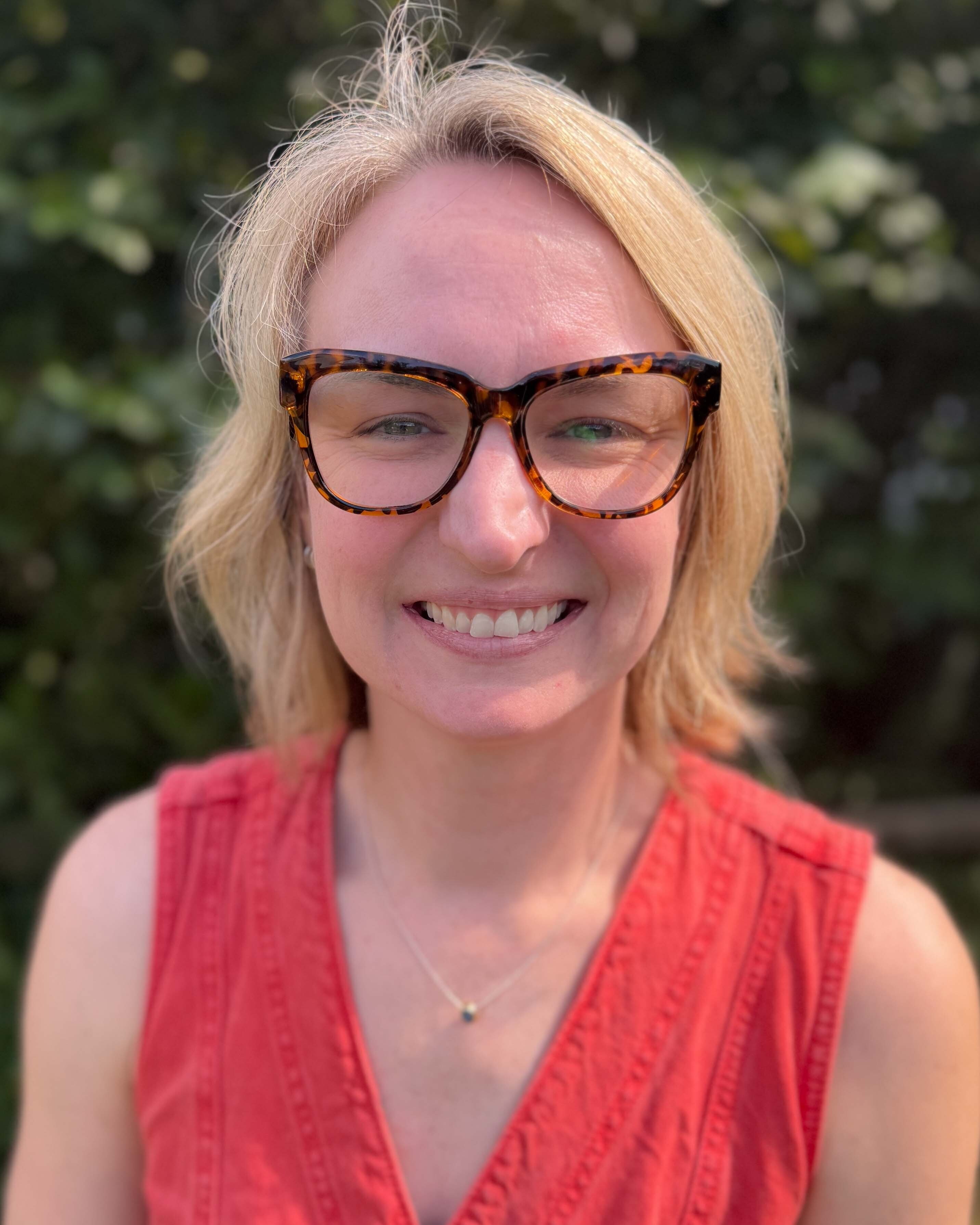 Wall Community Options director Erin Justis standing outside in a red shirt wearing glasses