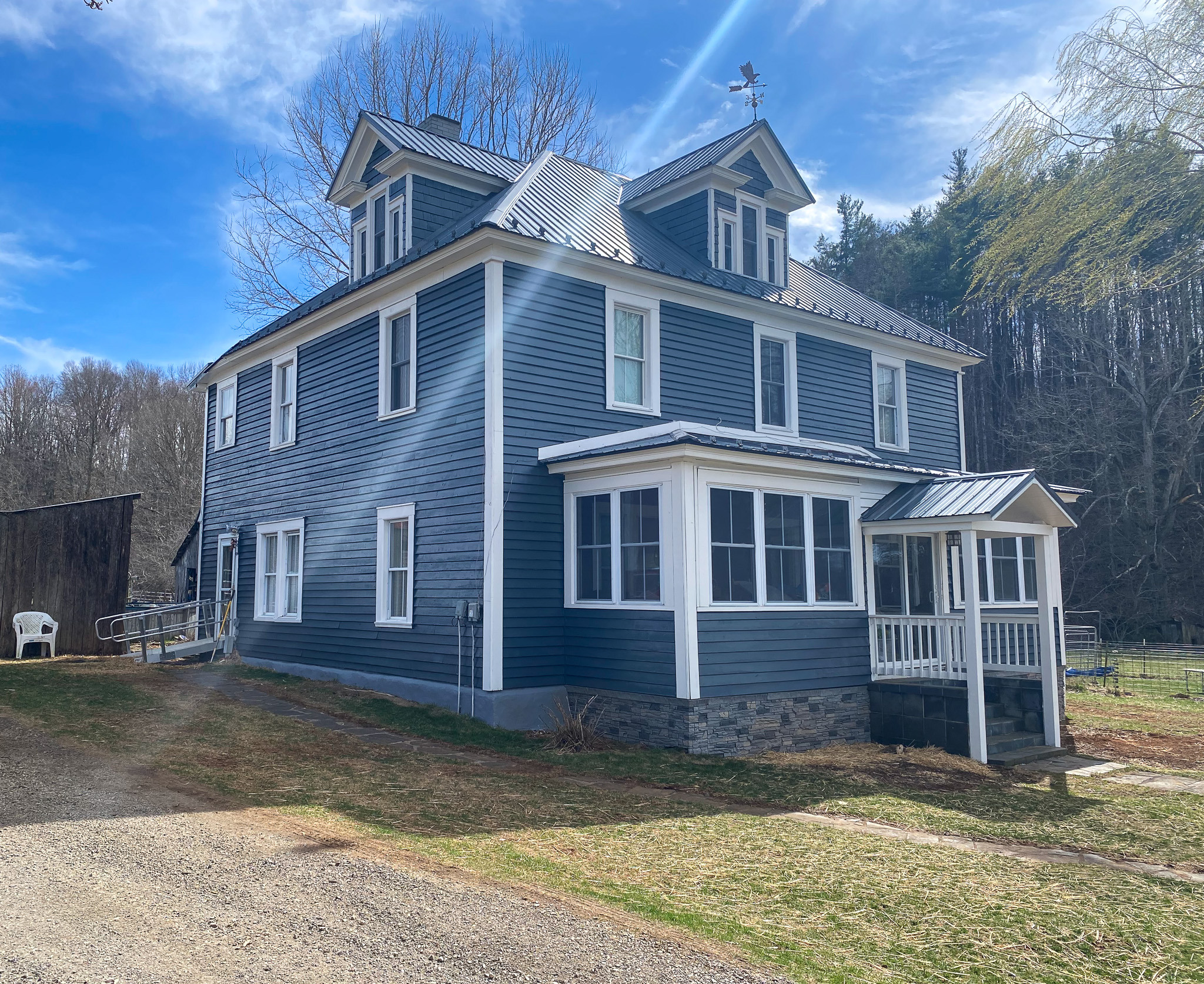 Two-story blue house with white trim, metal roof, small covered porch, and rural surroundings belonging to Sponsored Residential Providers Barbara and Larry Hatcher in Floyd, Virginia.