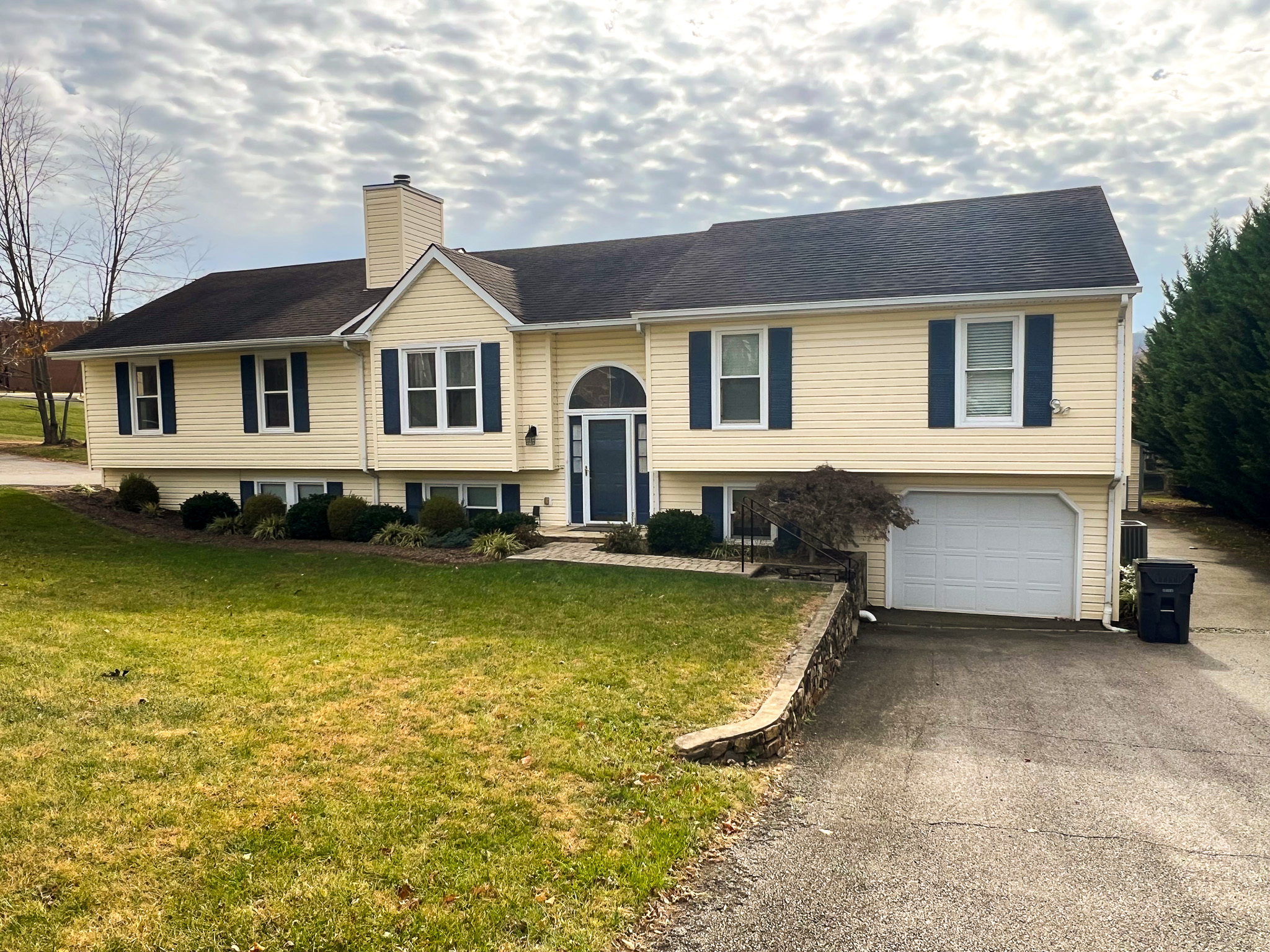 A light yellow split-level house with dark shutters, a central arched entryway, and an attached garage beside a paved driveway belonging to Group Home Providers Anthony and Melissa Johnson in Daleville, Virginia.