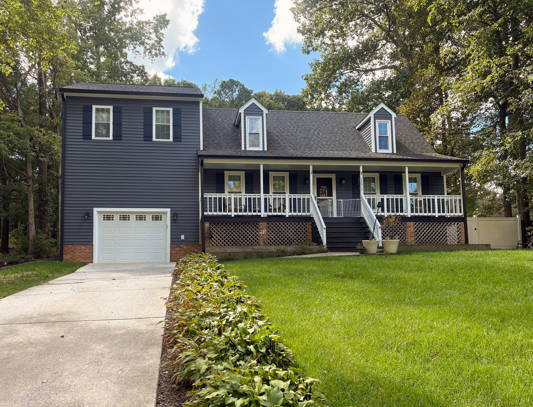 A dark blue two‑story house with white trim features a wide front porch, dormer windows, and a neatly maintained lawn leading up to the front steps belonging to Group Home Provider Lelia Mabry in Midlothian, Virginia.