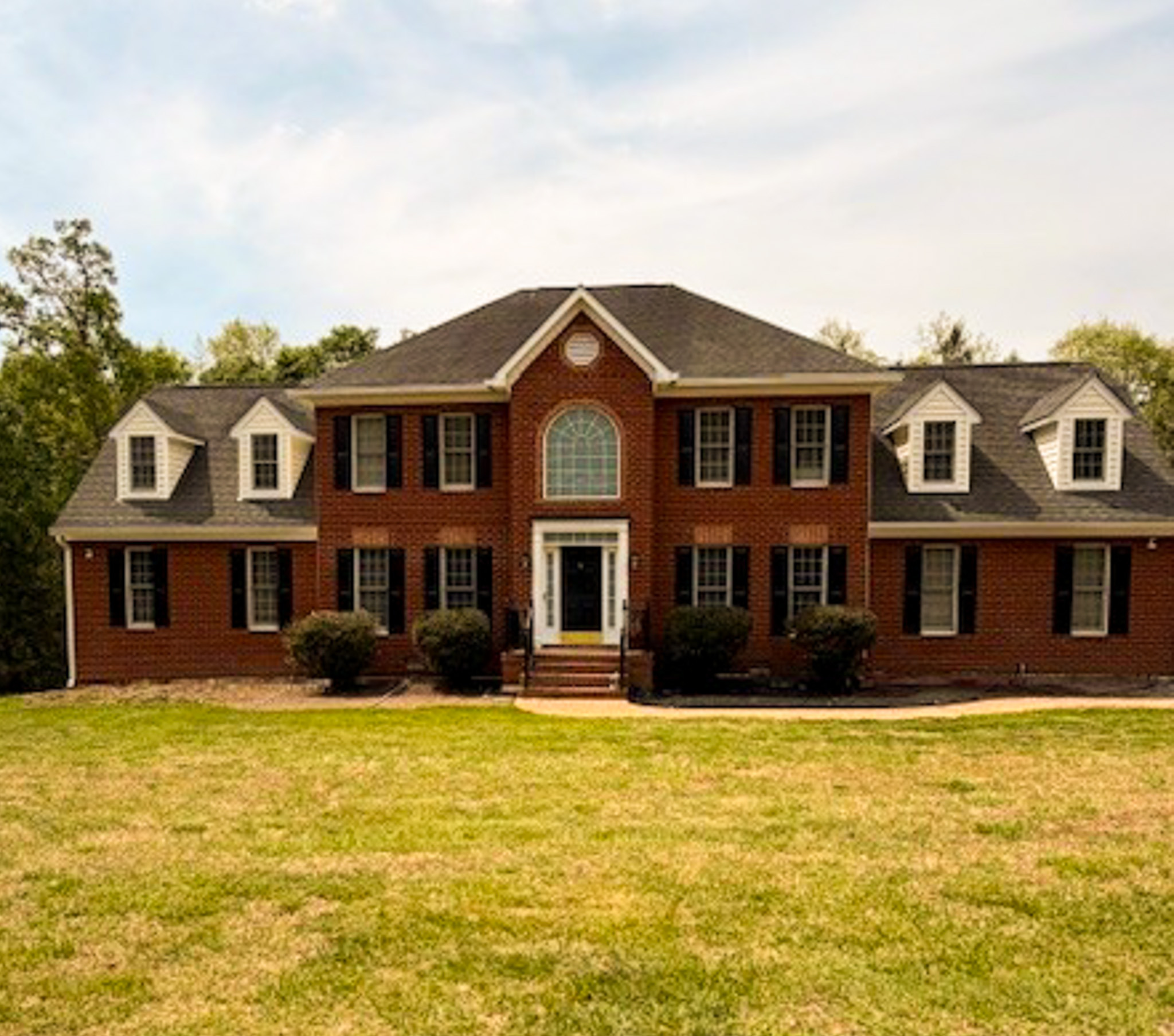 Two-story red brick house with black shutters, central arched window, and a large front lawn belonging to Sponsored Residential Provider Shirley Wright in Northern Virginia.
