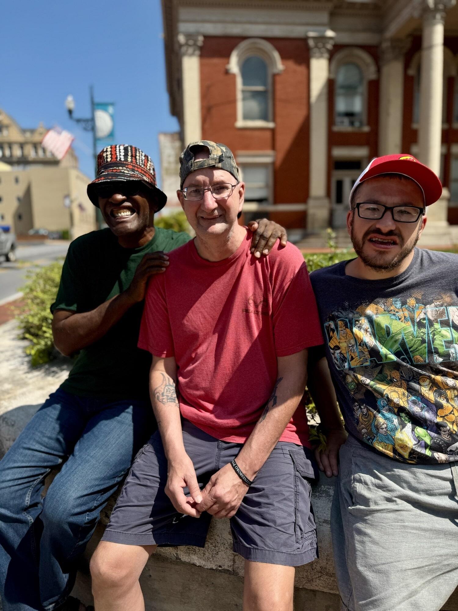 Three men sitting outside next to each other in a downtown area.