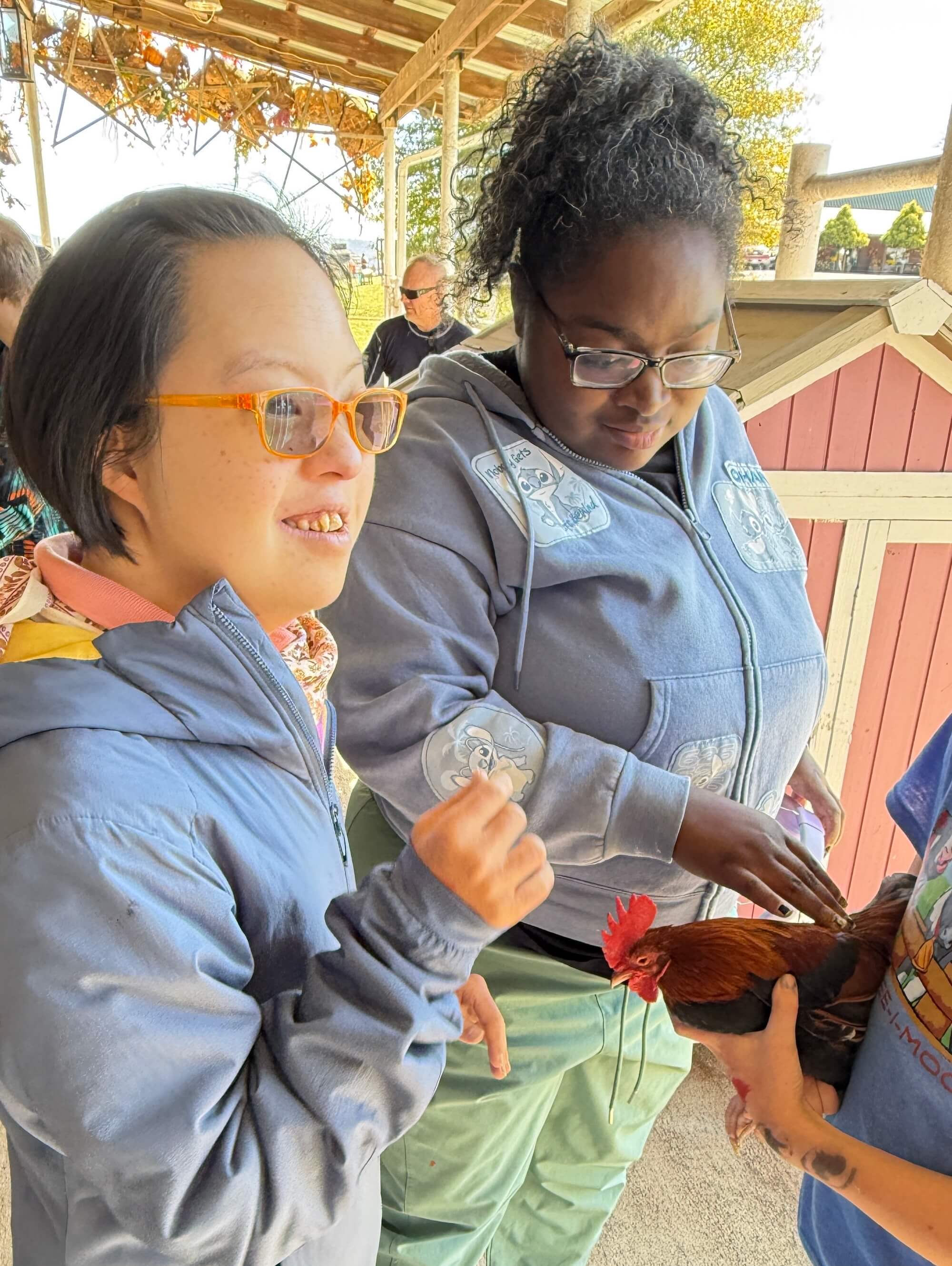 Two women outside smiling and petting a chicken