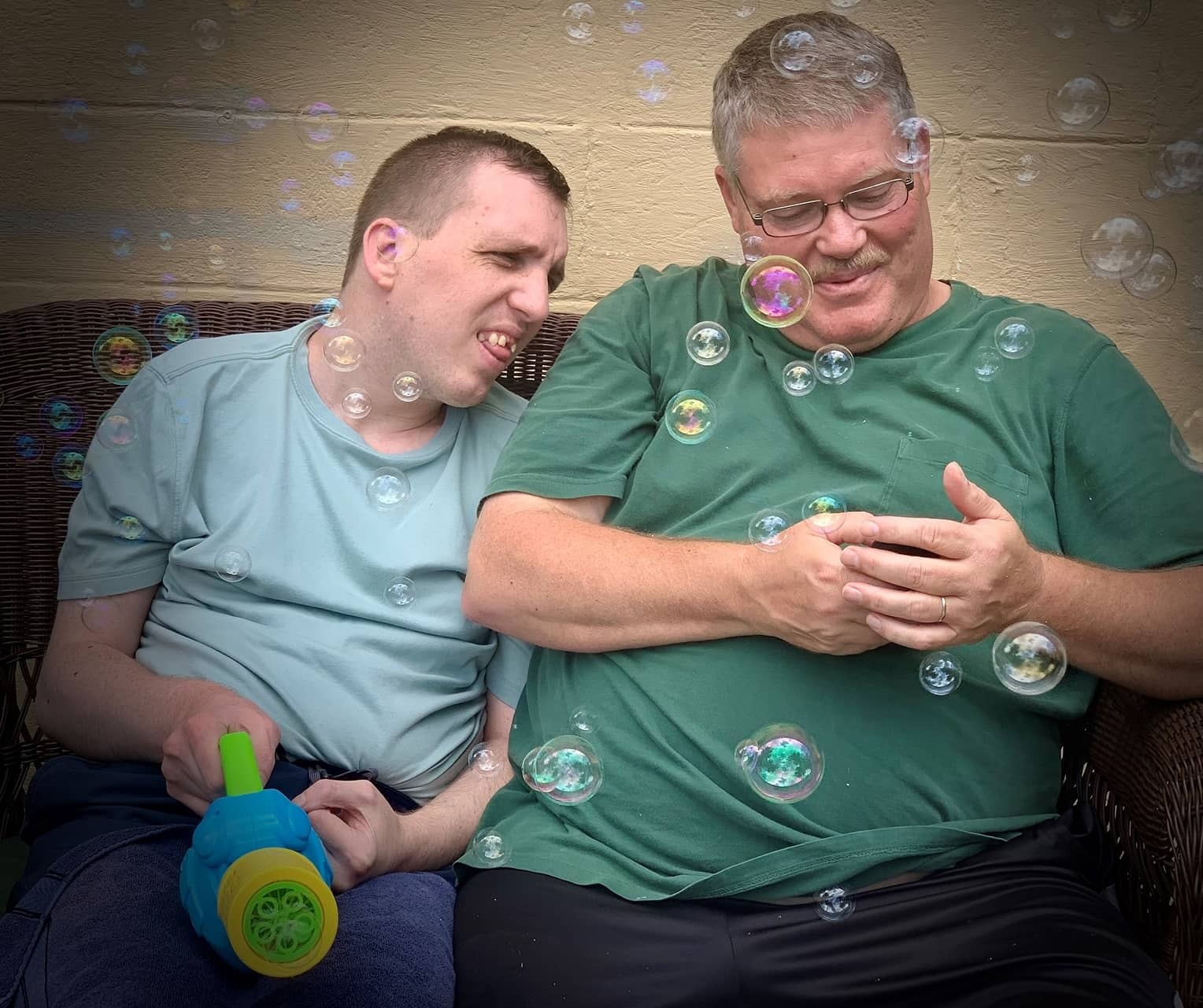 Individual holding a bubble gun sits next to Provider as both look at the Provider’s phone while surrounded by bubbles
